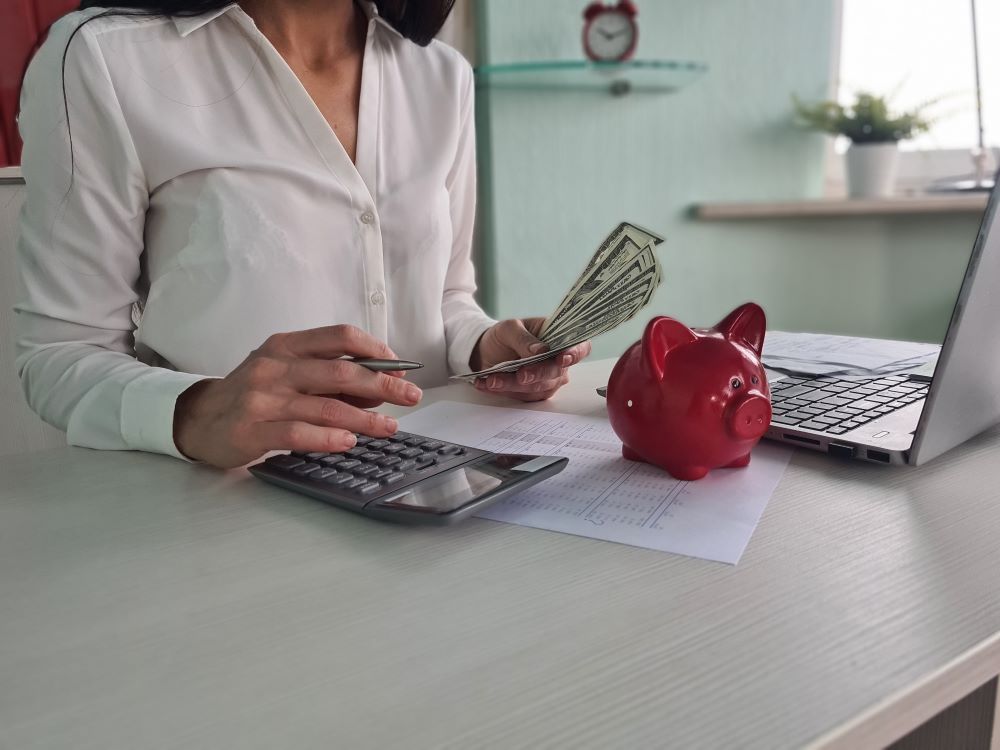 Pessoa contando dinheiro e usando calculadora ao lado de cofrinho, analisando valores relacionados ao dissídio.