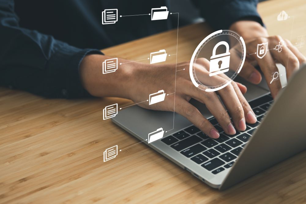 Pessoa utiliza notebook com símbolos de documentos, pastas e cadeado, representando a segurança de dados no departamento pessoal.
