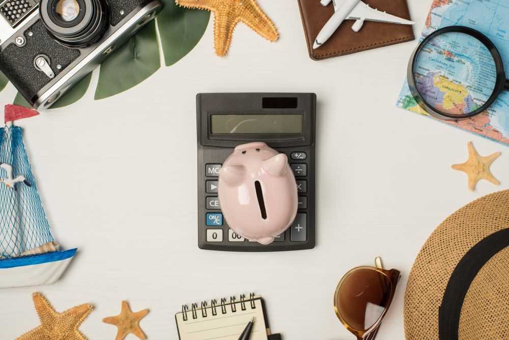 Calculadora com cofre em formato de porquinho cercada por itens de viagem.