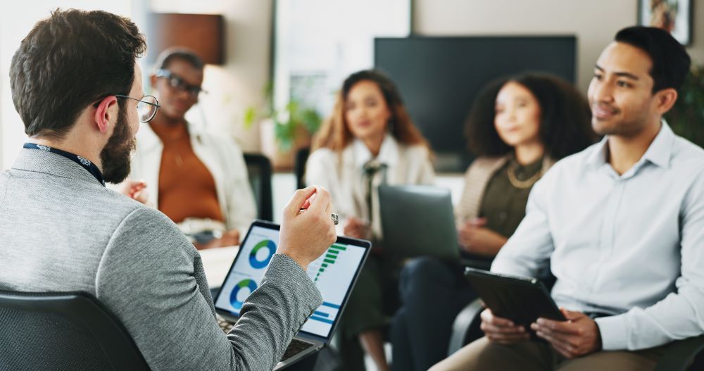 Equipe reunida em escritório analisando gráficos e indicadores em um notebook, representando planejamento e gestão de resultados relacionados ao PPR.